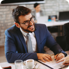 A businessman smiles as takes notes and speaks with a customer.